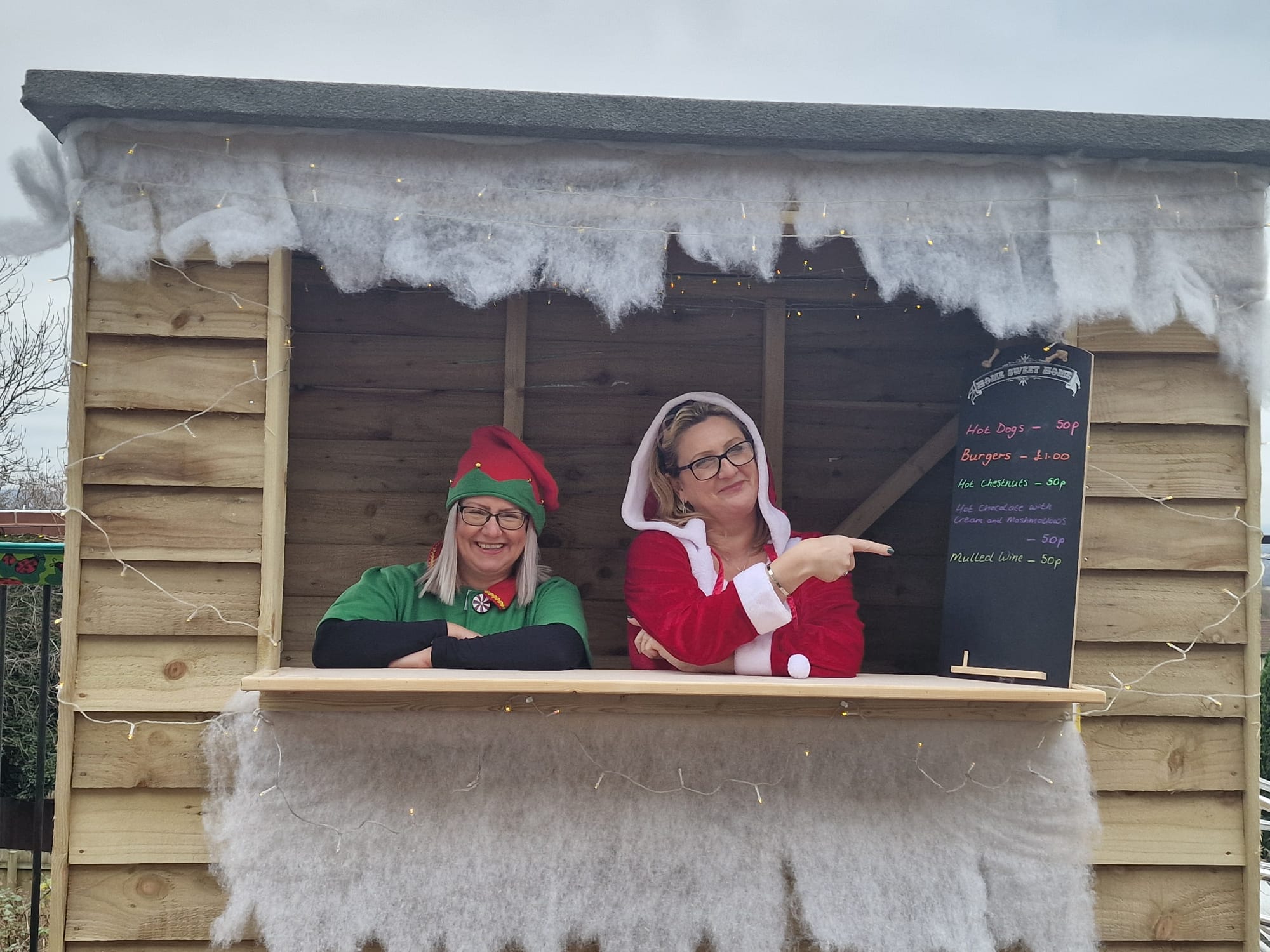 thistle court team members dressed as santa and an elf in a wooden foot hut at the christmas fayre